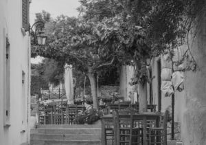 Black and white photo of café tables under trees on a Koukaki street